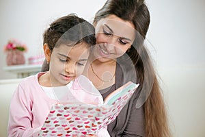 Cute little girl reading book with mother