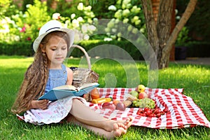 Cute little girl reading book outdoors