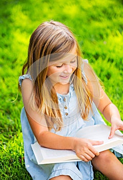 Cute little girl reading book outside on grass