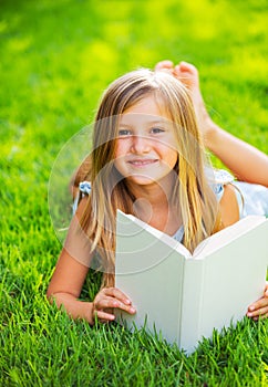 Cute little girl reading book outside on grass