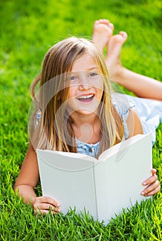 Cute little girl reading book outside on grass