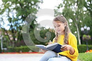 Cute little girl reading book in park