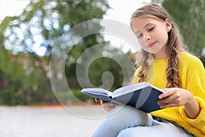 Cute little girl reading book in park