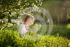 Cute little girl reading a book in a park on the grass in summer