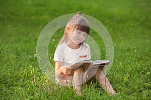 Cute little girl reading book in park on summer day