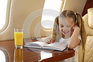 Cute little girl reading book at table in airplane during flight