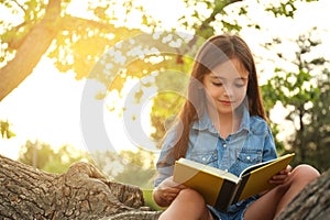 Cute little girl reading book on tree in park