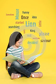 Cute little girl reading book on yellow background with word cloud