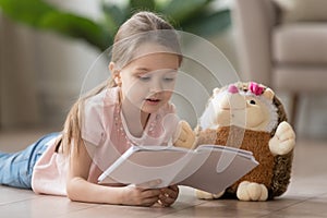 Cute little girl reading interesting book, lying on warm floor