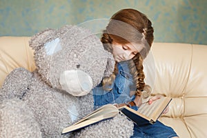 Cute little girl reading with teddy bear