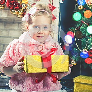 Cute little girl receive a gift near decorating Christmas tree.