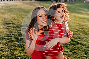 Cute little girl in red dress having fun in park with mom. Outdoor photo of blithesome woman playing