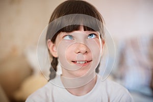 Cute little girl in a red dress with slanting eyes. The girl looks at the tip of her nose