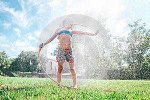 Cute little girl refresh herself from garden watering hose