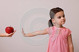 Cute little girl refusing to eat apple on grey background