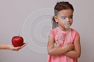 Cute little girl refusing to eat apple on grey background