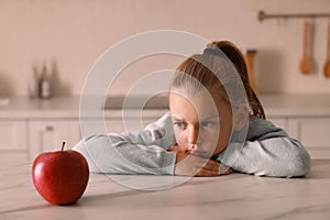 Cute little girl refusing to eat apple in kitchen