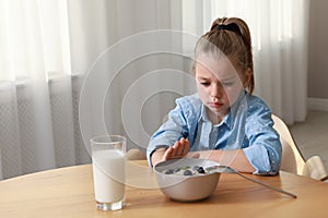 Cute little girl refusing to eat her breakfast at home, space for text