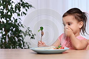 Cute little girl refusing to eat her breakfast at home, space for text