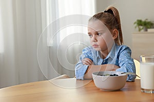 Cute little girl refusing to eat her breakfast at home, space for text