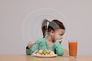 Cute little girl refusing to eat vegetable salad at table on grey background