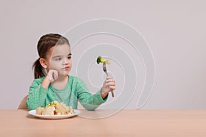 Cute little girl refusing to eat vegetable salad at table on grey background, space for text