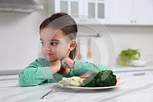 Cute little girl refusing to eat vegetables in kitchen