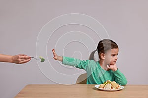 Cute little girl refusing to eat vegetables at table on grey background