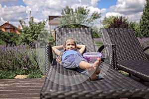 A cute little girl relaxing on the chaise longue at green garden outside, home feeling