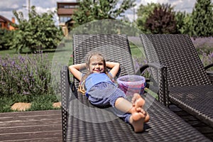 A cute little girl relaxing on the chaise longue at green garden outside, home feeling