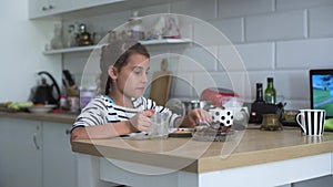Cute Little Girl Resting on a chair Uses Laptop, Watches Funny Videos and Cartoons . A Little girl sitting to eat a snack in a liv