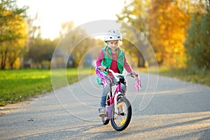 Cute little girl riding a bike in a city park on sunny autumn day. Active family leisure with kids.