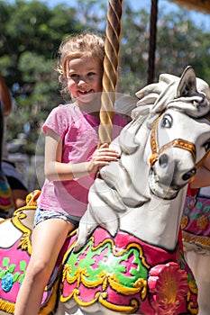 Cute little girl riding on a carousel in an amusement park in the summer.