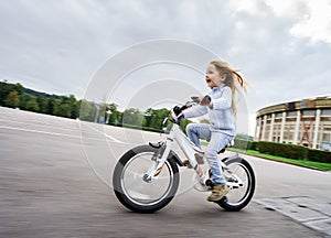 Cute little girl riding fast by bicycle