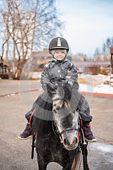 Cute little girl riding a little horse or pony in the winter on farm