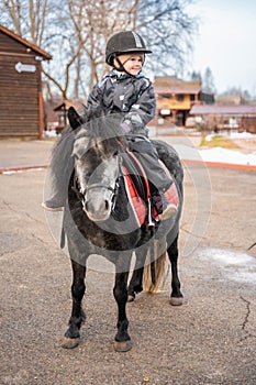 Cute little girl riding a little horse or pony in winter on farm