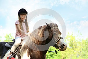 Cute little girl riding pony outdoors