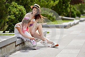 little girl on roller skates and her mother sitting in park.