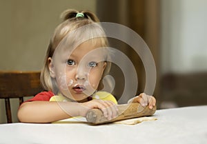 Cute little girl is rolling dough with wooden pin