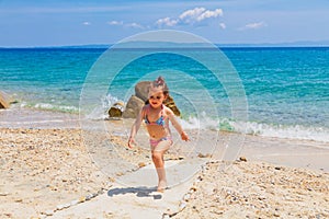 Cute little girl running at the beach near the sea on vacations