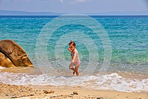 Cute little girl running at the beach near the sea on vacations