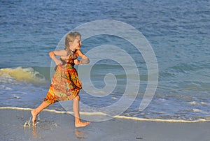 Cute little girl running on sandy beach in sunset