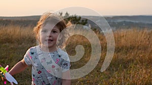 Cute Little Girl Running In The Field. She Has In Her Hands Toy Windmill Spinning From The Wind.