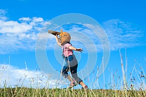 Cute little girl running through the meadow on a sunny day with a toy plane in hand. Happy kid playing with cardboard plane