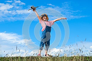 Cute little girl running through the meadow on a sunny day with a toy plane in hand. Happy kid playing with cardboard plane