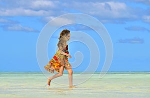 Cute little girl running on sandy beach in sunset