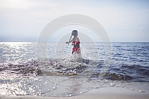 Cute little girl running into the sea in sunset light, lots of splashes and happiness