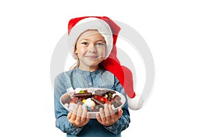 Cute little girl in santa hat with a plate of sweets isolated on white background. Happy child with lollipops and chocolate