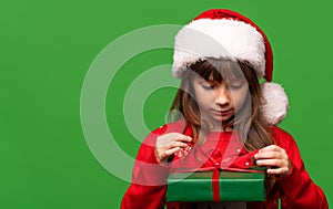 A cute little girl in a Santa hat unpacks a New Year's gift. Merry Christmas and Happy New Year 2023. Portrait