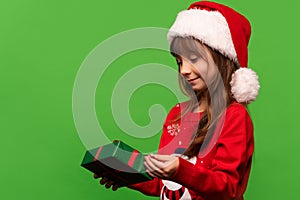 A cute little girl in a Santa hat unpacks a New Year's gift. Merry Christmas and Happy New Year 2023. Portrait